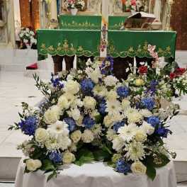 Low blue and white altar arrangement with roses and mums around a tall decorative candle
