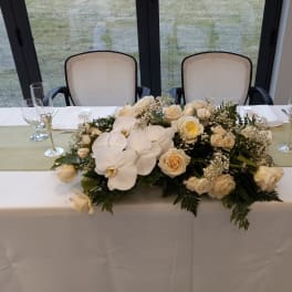 Low white floral centerpiece with roses and orchids on a table