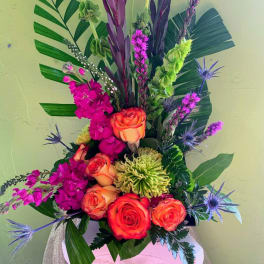 Tall tropical bouquet with orange roses, magenta blooms, and purple accents