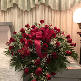 Heart-shaped spray of red roses with a pink ribbon on a casket