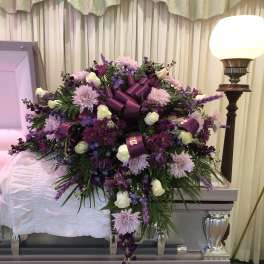 Purple and white floral casket spray with ribbon on a coffin