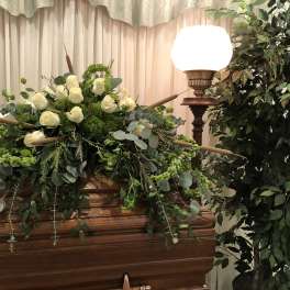 White rose casket spray with trailing greenery on a wooden casket
