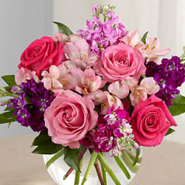 Pink roses and purple flowers arranged in a clear glass vase