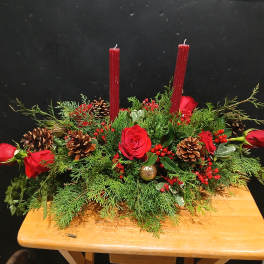 Red roses and candles in a low evergreen centerpiece with pinecones