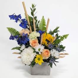 Mixed bouquet in a gray square vase with blue, white, yellow, and peach flowers