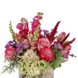 Mixed bouquet of pink, red, and purple flowers in a square glass vase