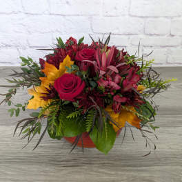Bouquet of red roses and burgundy flowers in a low orange container