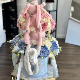 Pink plush bunny sitting on a box of pink and blue flowers
