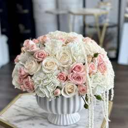 Round bouquet of blush and white roses in a white pedestal vase