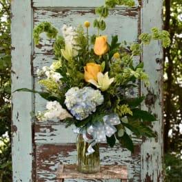 Bouquet of yellow roses, hydrangea, and white lilies in a glass vase