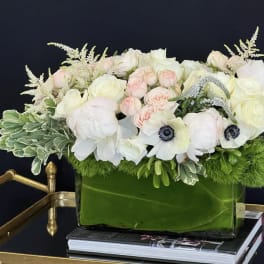 White and blush floral arrangement in a green glass vase