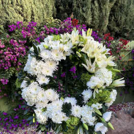 Large white floral wreath on a stand with lilies and chrysanthemums