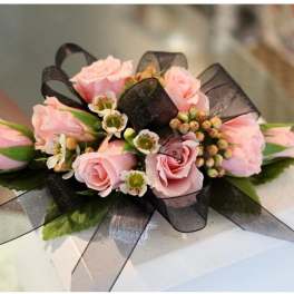 Corsage of pink roses with small white blossoms and black ribbon accents