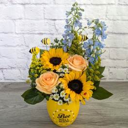 Sunflowers and peach roses in a yellow vase with bee decorations