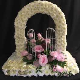 White floral funeral arch with pink roses and a cross topper