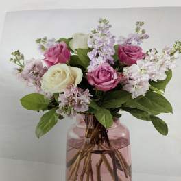 Pink and white roses with lavender blooms in a pink glass vase