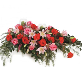 Casket spray with red and pink roses and pale lilies