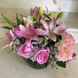Pink lilies and roses arranged with pale hydrangea in a low vase
