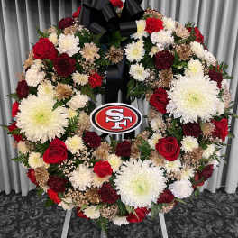 Standing round wreath of white mums and red roses with team logo center and black bow on an easel