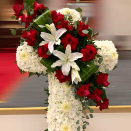Tall white floral cross with red roses and white lilies accenting the upper side