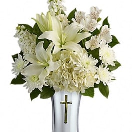 White lilies and daisies arranged in a silver vase with a cross
