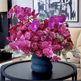 Pink orchids and roses arranged in a dark vase on a table
