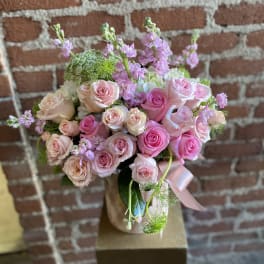Pink and peach rose arrangement with soft pink accent flowers in a blush vase with ribbon