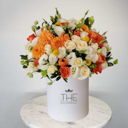 Orange and white flower arrangement in a white hat box