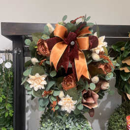 Fall wreath with orange ribbon, cream flowers, and eucalyptus on a dark frame