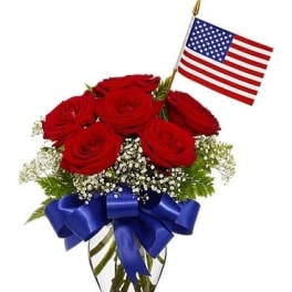 Red roses in a glass vase with a blue ribbon and small American flag