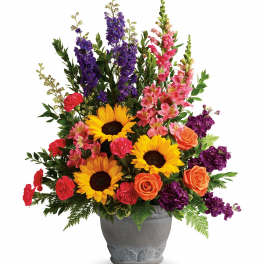 Mixed bouquet with sunflowers, roses, carnations, and purple spikes in a gray vase
