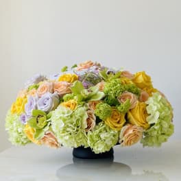 Low floral arrangement with roses, hydrangeas, and orchids in a black vase