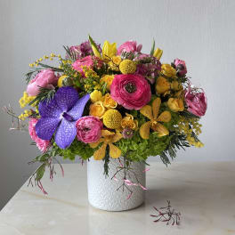 Bright mixed bouquet in a white textured vase with pink, yellow, and purple blooms