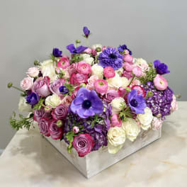 Mixed pink, white, and purple flowers arranged in a white wooden box