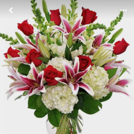 Vase arrangement of red roses, pink lilies, and white hydrangeas in a clear glass vase