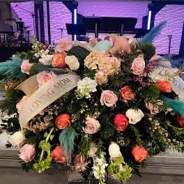 Large casket spray of pink, peach, and white roses with ribbons reading Loving Mom and Loving Nana.