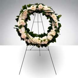 Circular floral wreath of cream roses and white blooms on a black stand