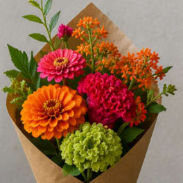 Bright mixed bouquet of zinnias and small orange flowers wrapped in brown paper