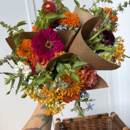 Handheld bouquets of bright mixed flowers wrapped in brown paper