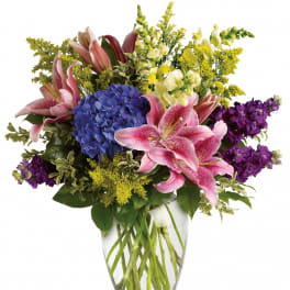 Bouquet of pink lilies, blue hydrangea, and purple flowers in a clear glass vase