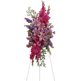 Tall standing floral spray with pink lilies and purple flowers on a white easel