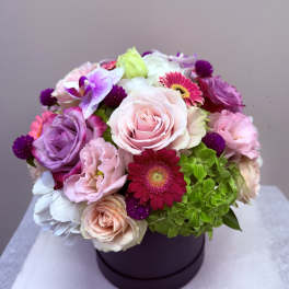 Mixed pink, purple, and white flowers arranged in a round box