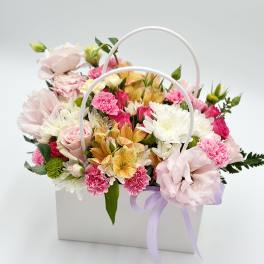Pastel flower arrangement in a white handled box with a lavender ribbon