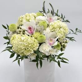 White and pale green floral arrangement in a white vase with pink orchid accents