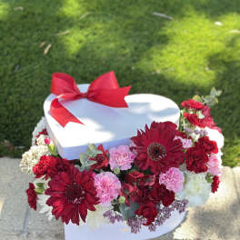 Heart-shaped white gift box with red ribbon and red, pink, and white flowers
