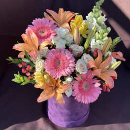 Pink gerberas, peach lilies, and white roses in a purple hat box