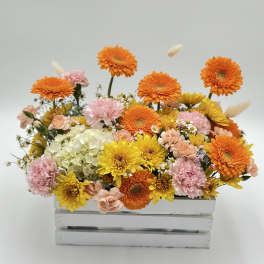 Bright mixed flower arrangement in a white wooden crate