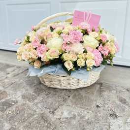 Basket of pale pink and cream roses with carnations and a pink card