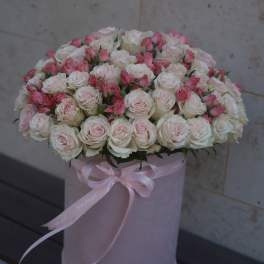 Pink and white roses arranged in a round hatbox with a ribbon bow