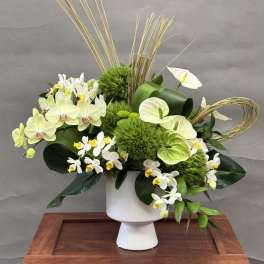 White and green floral arrangement in a white pedestal vase